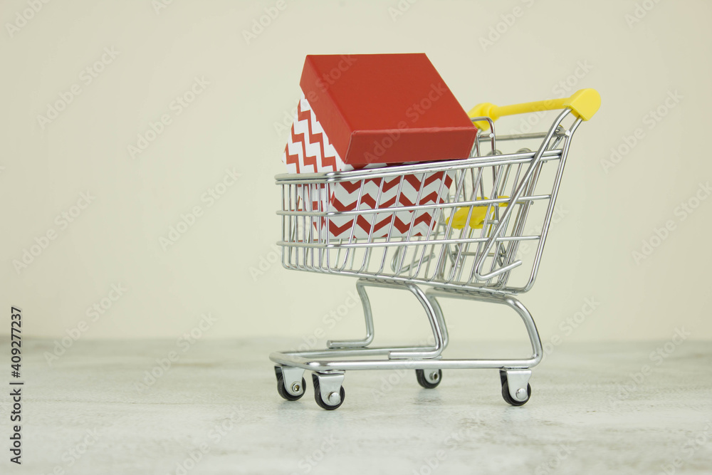 Mini shopping cart with a gift white and red box on a white background. Shopping concept