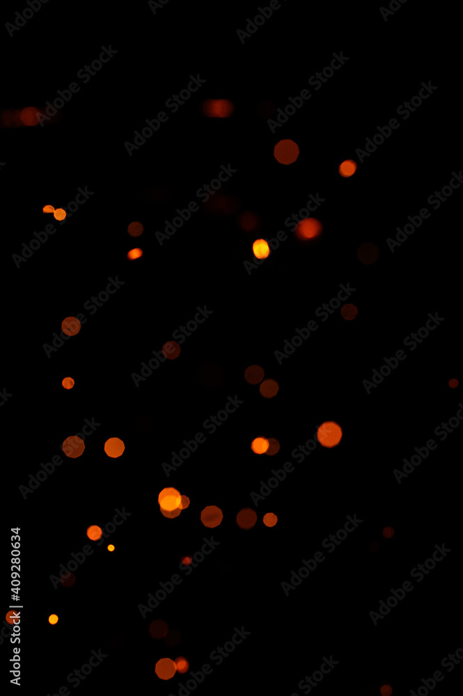 Orange bokeh on a black background, burning and blurred sparks from the fire. Particles of burning embers fly and glow isolated in the night sky. Orange bokeh on a black background, burning and blurred sparks from the fire. Particles of burning embers fly and glow isolated in the night sky.