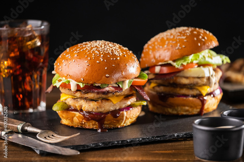 Yummy grilled chicken burger with double cutlet, fries and cola on a wooden table, side view. Hamburger and French fries. Fast food concept.