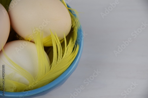 Easter eggs in blue bowl, yellow faethers on white wooden background with place for text photo