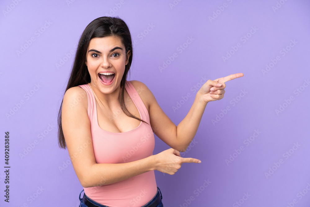 Young woman over isolated purple background surprised and pointing side Young woman over isolated purple background surprised and pointing side