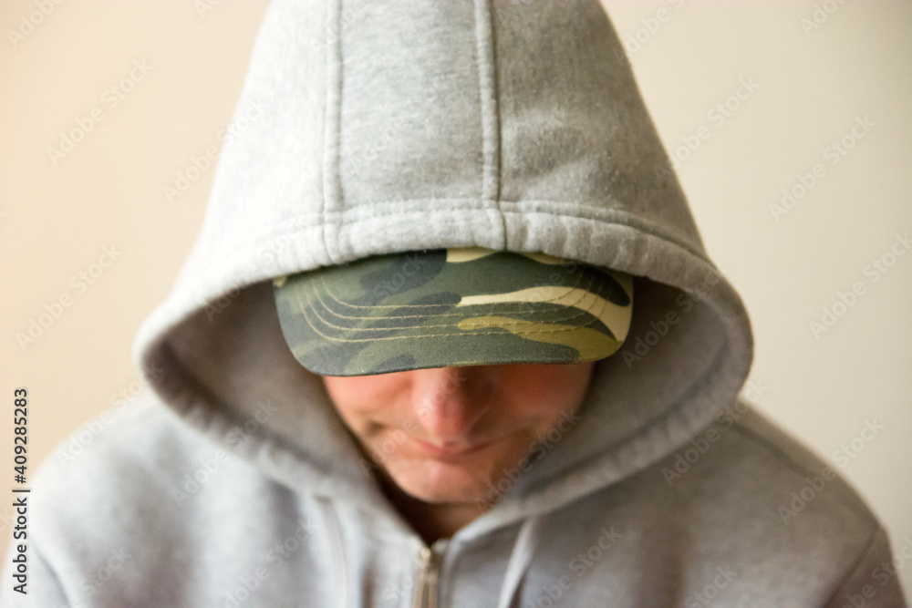 A man in a military baseball cap and a grey hooded sweatshirt, looking down A man in a military baseball cap and a grey hooded sweatshirt, looking down