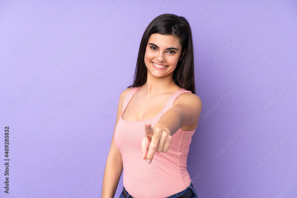 Young woman over isolated purple background points finger at you with a confident expression Young woman over isolated purple background points finger at you with a confident expression