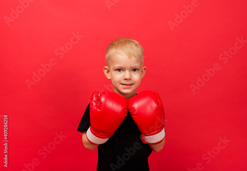 a little boy sportsman in red boxing gloves on a red background with space for text © Яна Айбазова