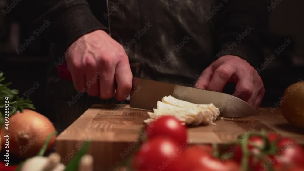 A man chef cuts cheese on a cutting board among fresh vegetables. Close-up of hands. A man chef cuts cheese on a cutting board among fresh vegetables. Close-up of hands.