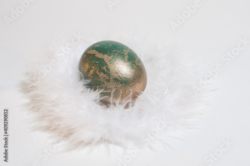 gold and green easter egg on white feathers