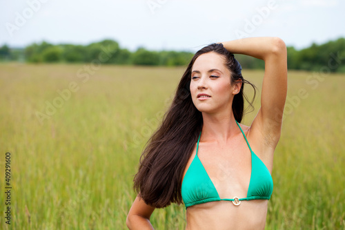 Beautiful model in a green bathing suit standing in the summer field