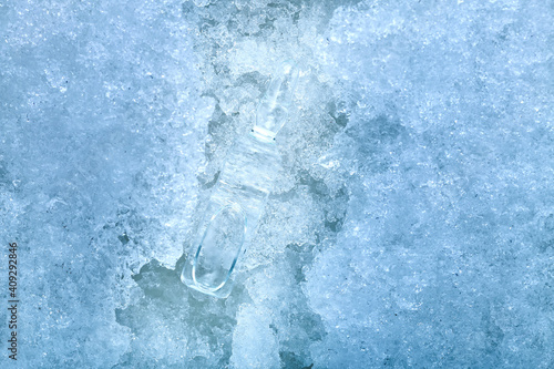 vaccine in a glass transparent ampoule with a medical product for vaccination against coronavirus disease chilled to subzero temperatures lying on cold ice closeup background on medical theme, nobody.