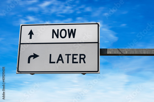 Road sign with words now and later. White two street signs with arrow on metal pole. Directional road, Crossroads Road Sign, Two Arrow. Blue sky background
