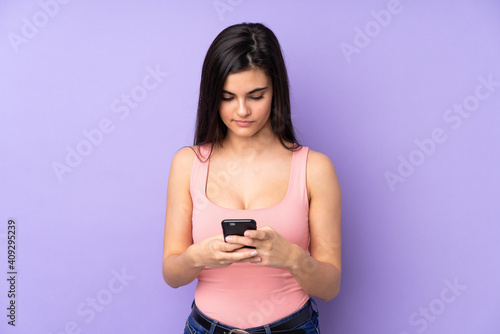 Young woman over isolated purple background sending a message with the mobile