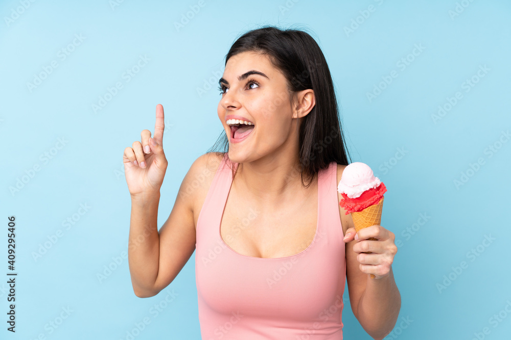 Young woman holding a cornet ice cream over isolated blue background intending to realizes the solution while lifting a finger up Young woman holding a cornet ice cream over isolated blue background intending to realizes the solution while lifting a finger up