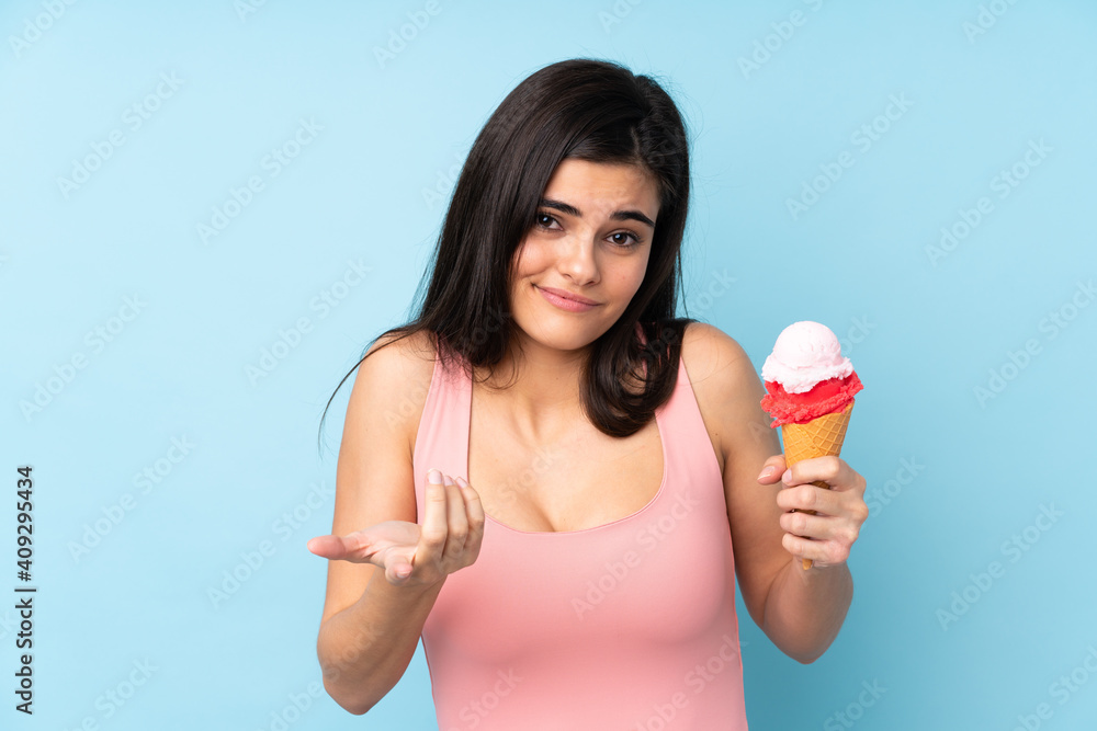 Young woman holding a cornet ice cream over isolated blue background making doubts gesture while lifting the shoulders Young woman holding a cornet ice cream over isolated blue background making doubts gesture while lifting the shoulders
