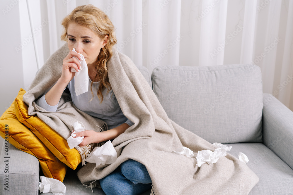 Sick young woman covered with blanket, sitting with napkin Sick young woman covered with blanket, sitting with napkin