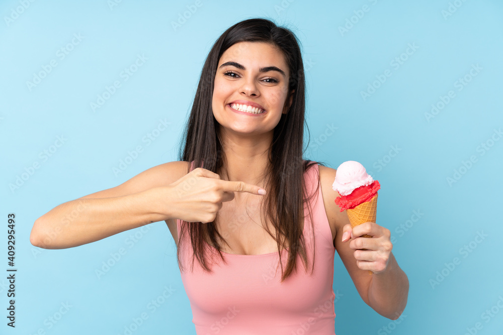 Young woman holding a cornet ice cream over isolated blue background and pointing it Young woman holding a cornet ice cream over isolated blue background and pointing it