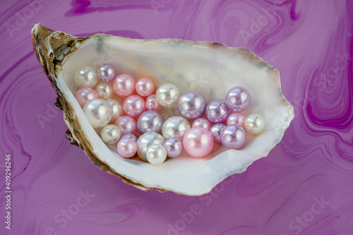 Artificial pearls inside the oyster shell. Different colors and size of pearls. Isolated on a rose background.