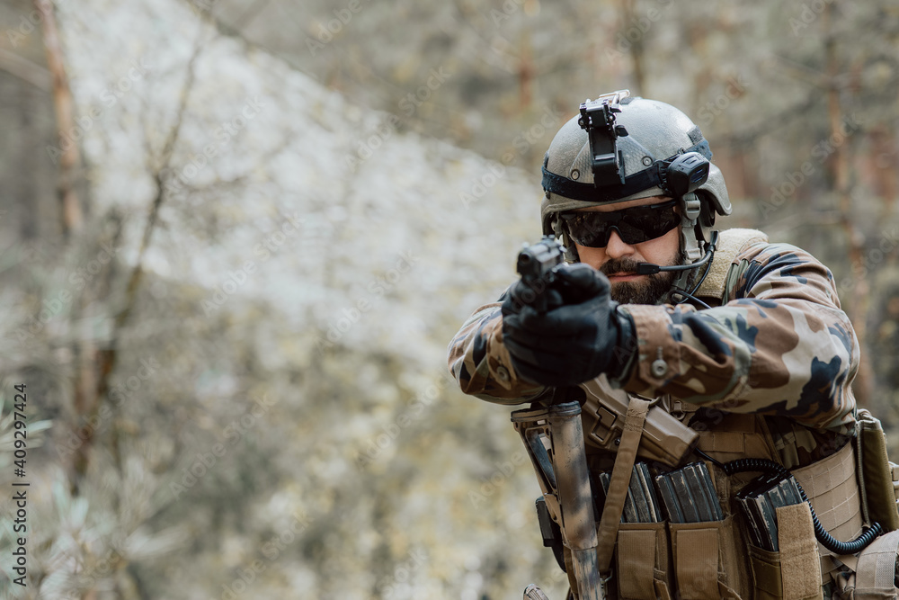 Obraz premium Portrait of a middle-aged bearded soldier in a Woodland military uniform and helmet, with headphones on his head holding a gun.