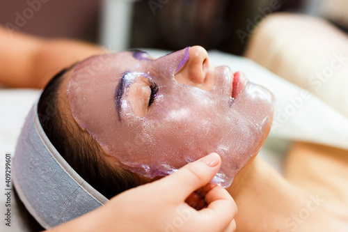 The beautician applies a transparent jelly peer mask to the girl's face. Facial skin care. Pore ​​removal and skin exfoliation.