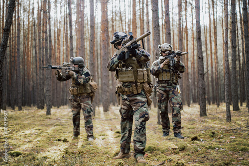 Fotografering Squad of Four Fully Equipped Soldiers in Camouflage on a Reconnaissance Military Mission, Aiming Rifles