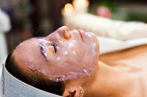 The cosmetologist for procedure of cleansing and moisturizing the skin, applying a sheet mask to the face of a young woman in beauty salon.Cosmetology and professional skin care.