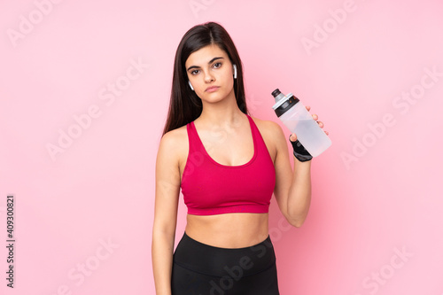 Young sport woman over isolated pink background with sports water bottle © luismolinero