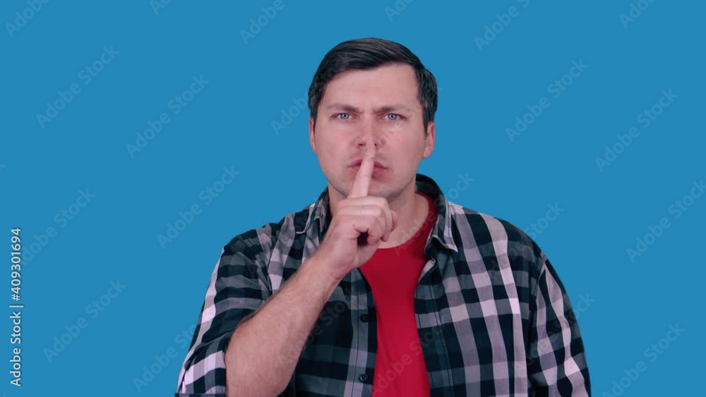 Man makes Shhh quiet, silence, secret gesture, isolated on a blue wall background. Man makes Shhh quiet, silence, secret gesture, isolated on a blue wall background.