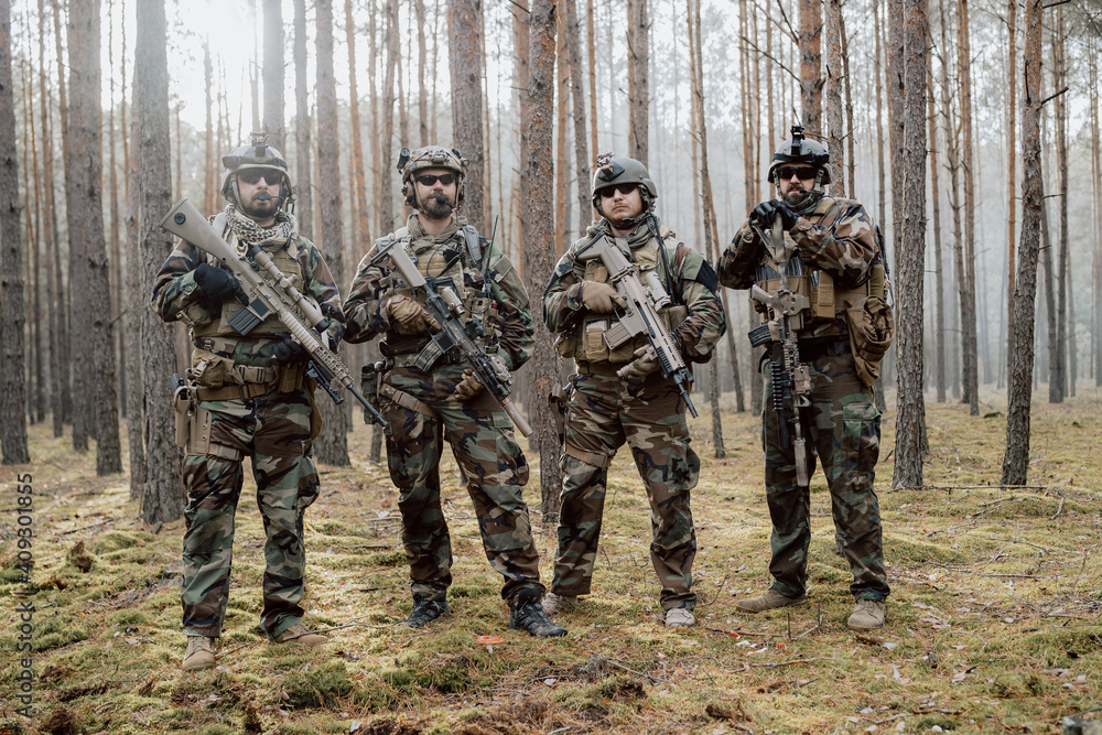 Fototapeta premium Portrait of a middle-aged bearded soldiers in a Woodland military uniform and helmet, with headphones on his head holding a rifle.