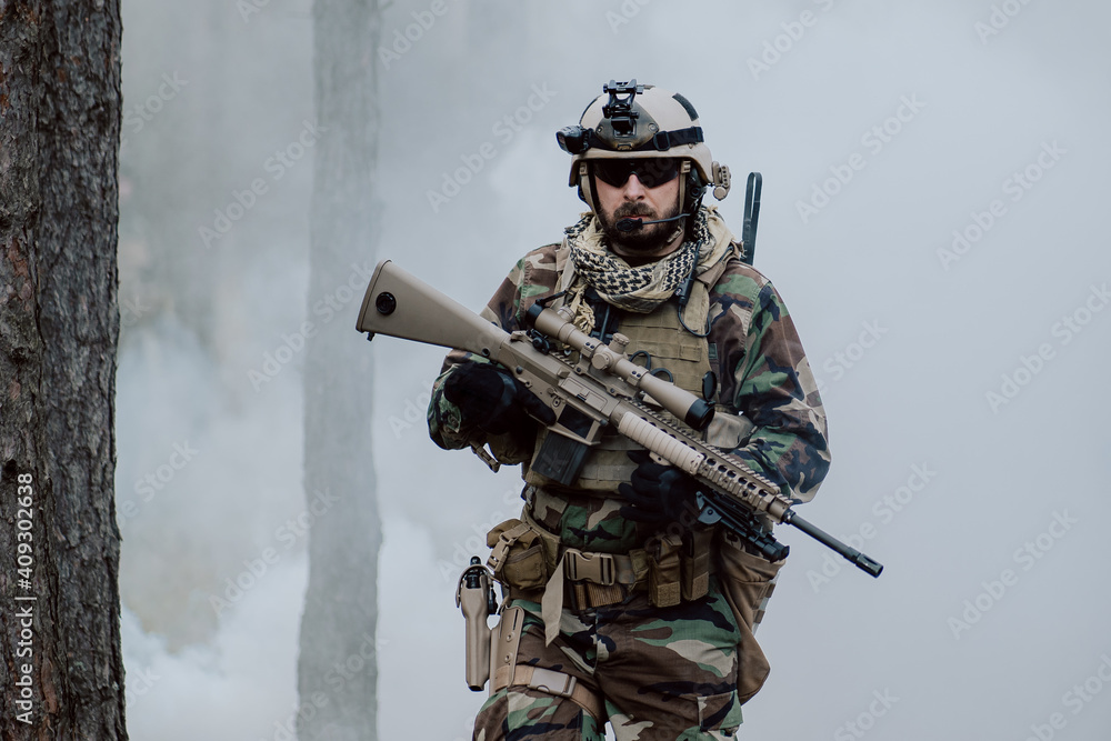 Fully equipped soldier in a camouflage uniform emerging from a puff of smoke in the middle of a pine forest. Fully equipped soldier in a camouflage uniform emerging from a puff of smoke in the middle of a pine forest.