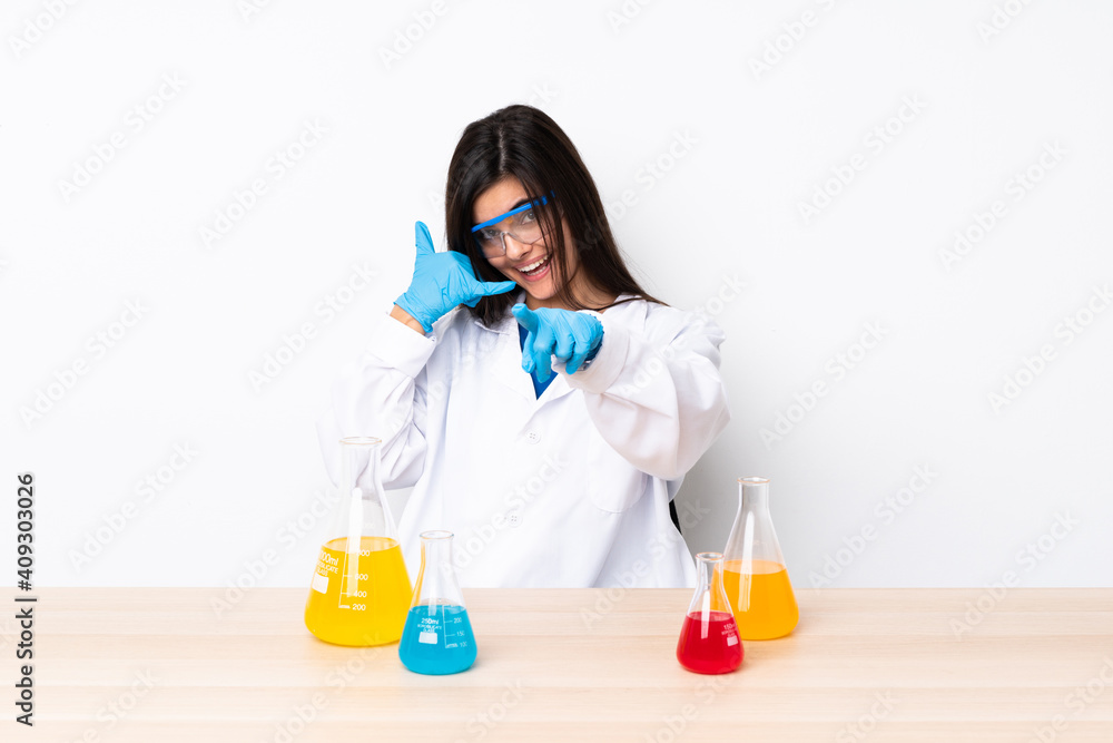 Young scientific woman in a table making phone gesture and pointing front Young scientific woman in a table making phone gesture and pointing front