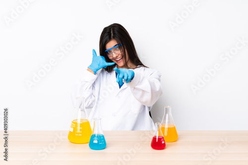 Young scientific woman in a table making phone gesture and pointing front