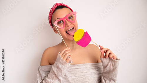 Woman with heart-shaped glasses on a stick eats fake paper craft cupcake. 