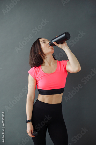 A woman in a sporty image on a gray background drinks water © nagornyak
