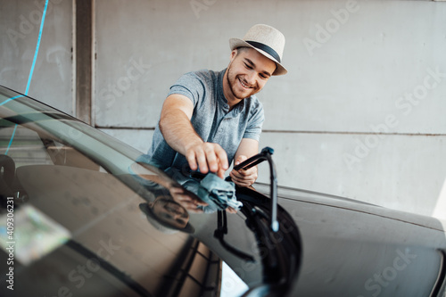 Young handsome man with hat cleaning car with rag, car detailing (or valeting) concept. © Dusko