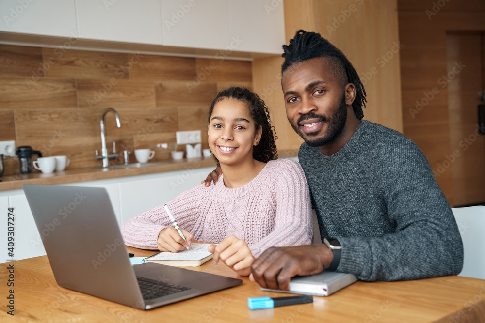 Obraz premium Happy African American father helps to study online to his teen age daughter.