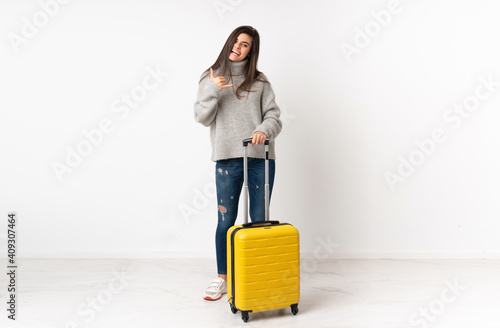 A full length body of a traveler woman with a suitcase over isolated white wall making phone gesture