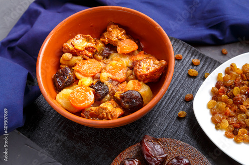 Jewish cuisine dish sweet zimmes with dates, carrots and turkey meat in a brown plate on a black board on a blue background near raisins and dates.