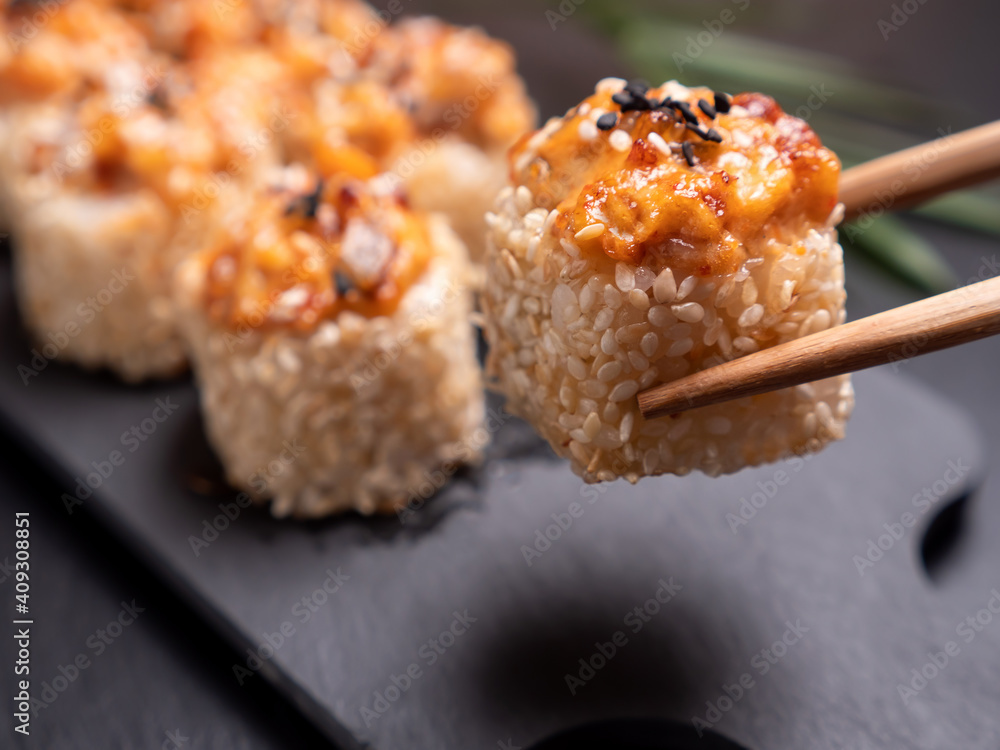 Take one Sushi roll with baked eel from black slate plate. One piece in chopsticks Take one Sushi roll with baked eel from black slate plate. One piece in chopsticks