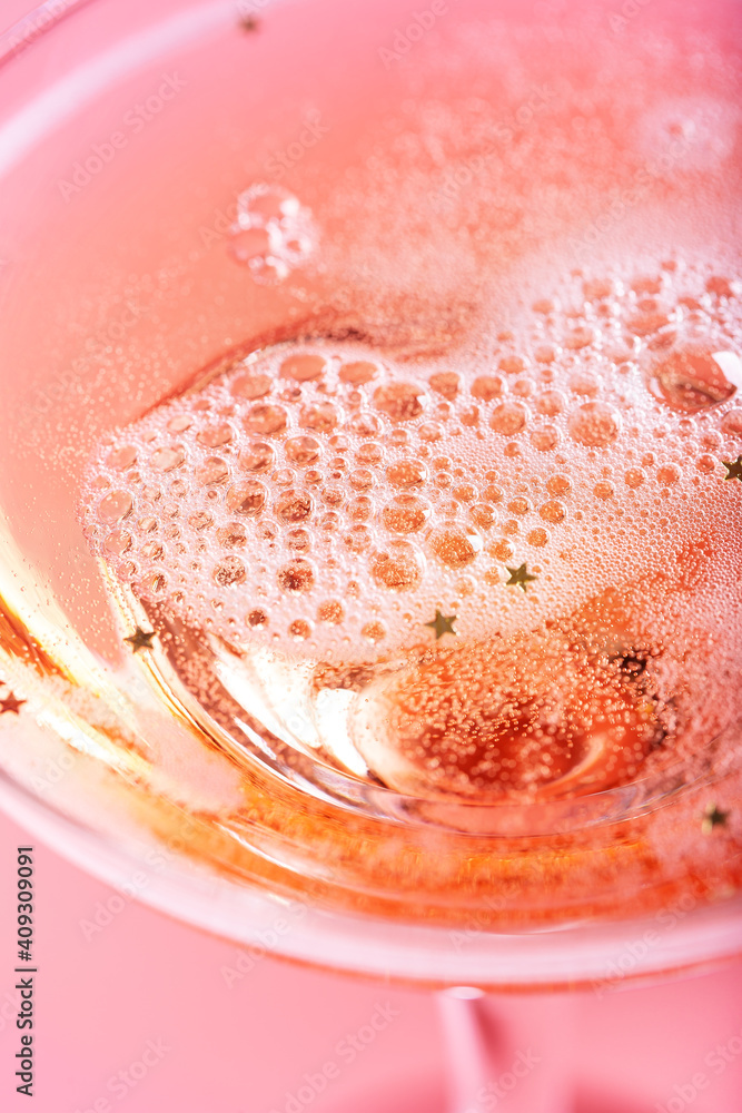 Fototapeta premium Closeup of glass with sparkling rose wine on pink background