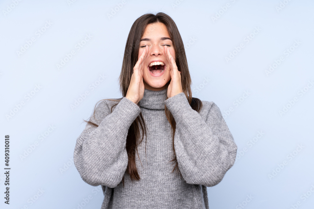 Teenager Brazilian girl over isolated blue background shouting and announcing something Teenager Brazilian girl over isolated blue background shouting and announcing something