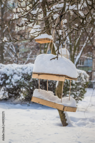 The bird feeder is covered with snow near the school. Wooden bird table topped with fresh snow