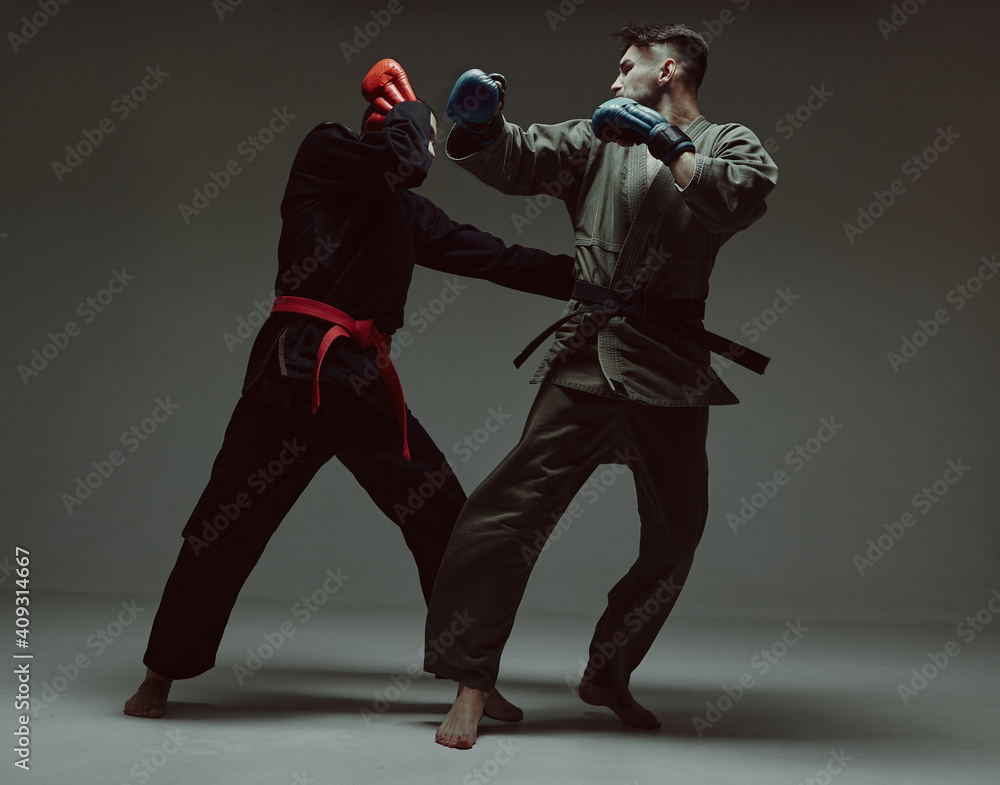 Fighting guys during mixed fight workout. Athletic males in kimono and boxing gloves training martial arts technique 