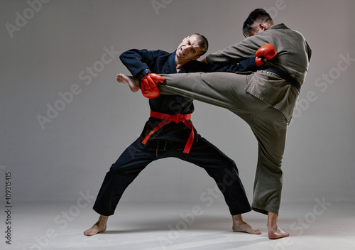 Athletic guys fighting, wearing kimono and boxing gloves on gray studio background with copy space, mixed fight concept
