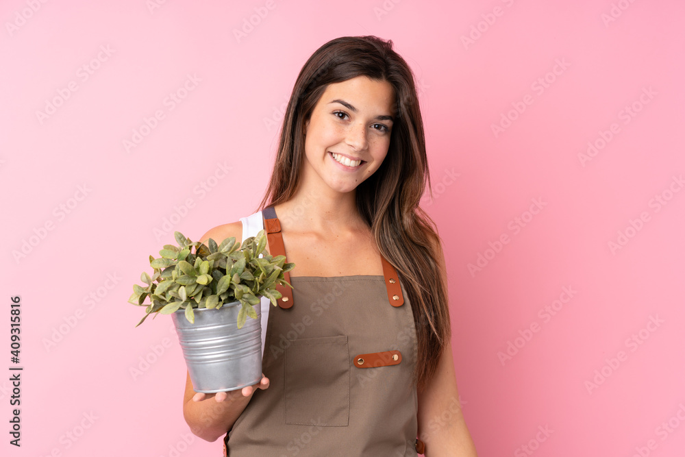 Teenager gardener girl holding a plant over isolated pink background smiling a lot Teenager gardener girl holding a plant over isolated pink background smiling a lot