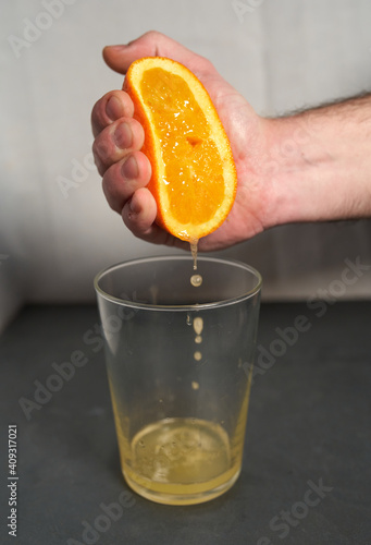 Male hand squeezing an orange into a glass.