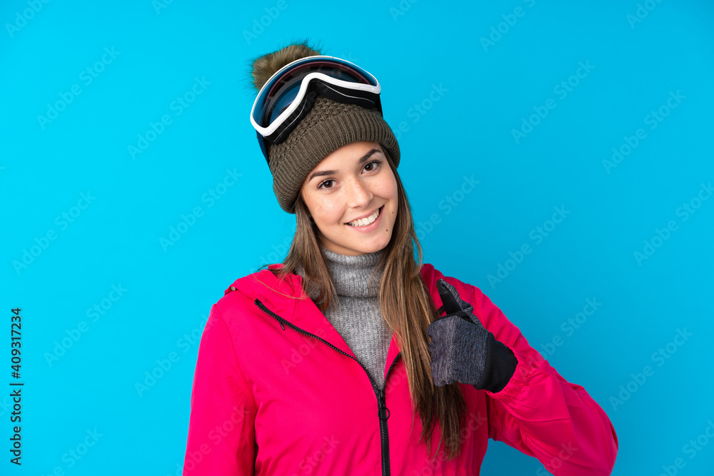 Teenager skier girl with snowboarding glasses over isolated blue background giving a thumbs up gesture Teenager skier girl with snowboarding glasses over isolated blue background giving a thumbs up gesture