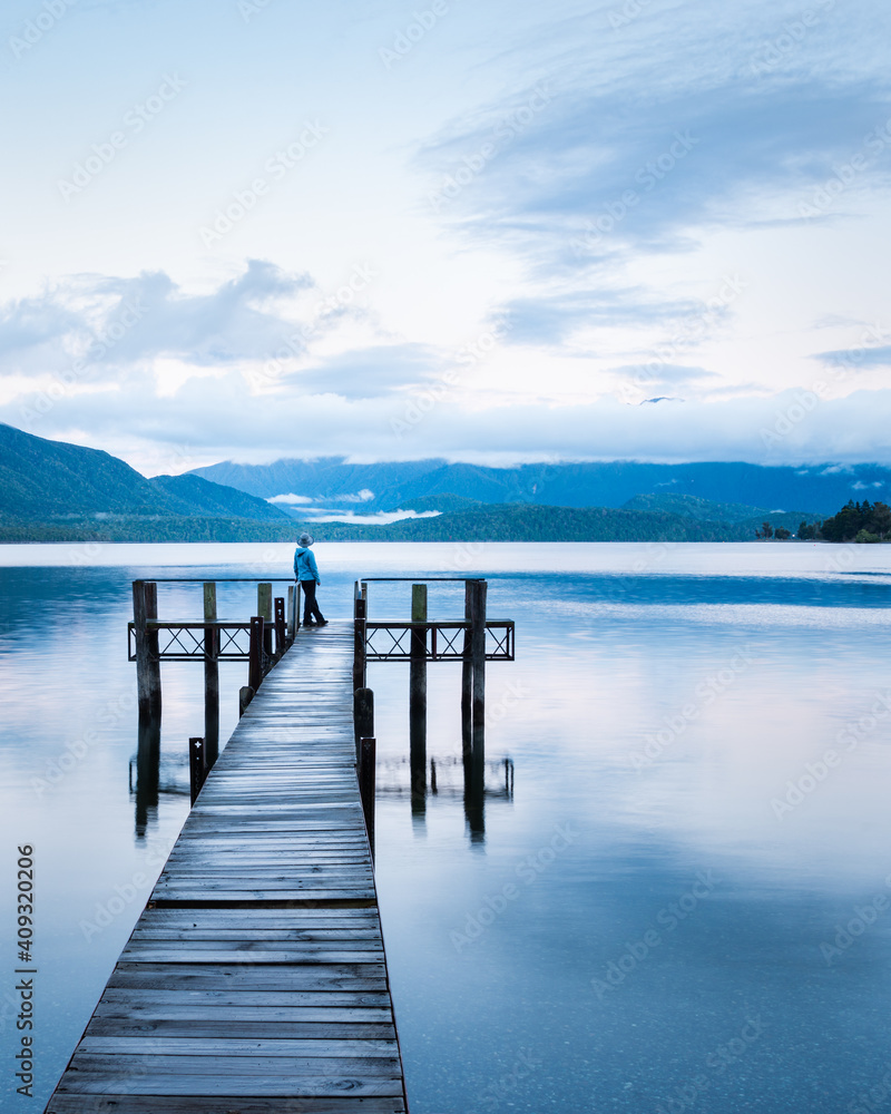 Lonely woman standing at the end of Lake Te Anau jetty, looking at the Kepler mountains. Vertical format.