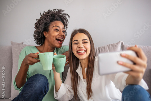 Shot of a two female friends taking selfie in the apartment. My roomies. Shot of two young women taking a selfie while sitting at home. Shared Living: roommates make a selfie photo