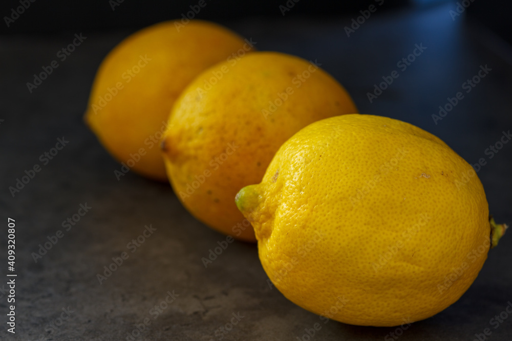 Drei Zitronen hintereinander aufgelegt versetzt auf dunklem Hintergrund