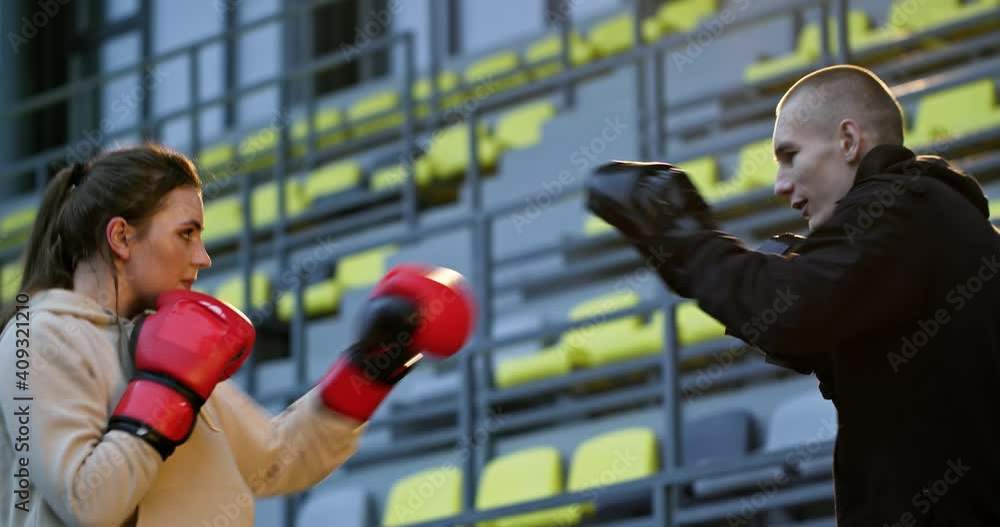 Personal training of a young boxing coach with a strong girl who is preparing for a fight practicing punches in boxing gloves on the street in sportswear Personal training of a young boxing coach with a strong girl who is preparing for a fight practicing punches in boxing gloves on the street in sportswear