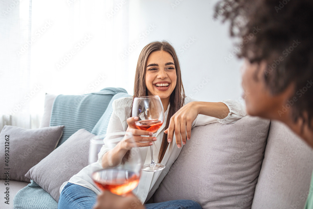 Two Female Friends Relaxing On Sofa At Home With Glass Of Wine Talking Together. Friends spending time talking and drinking wine. Shot of two friends talking together and drinking wine Two Female Friends Relaxing On Sofa At Home With Glass Of Wine Talking Together. Friends spending time talking and drinking wine. Shot of two friends talking together and drinking wine