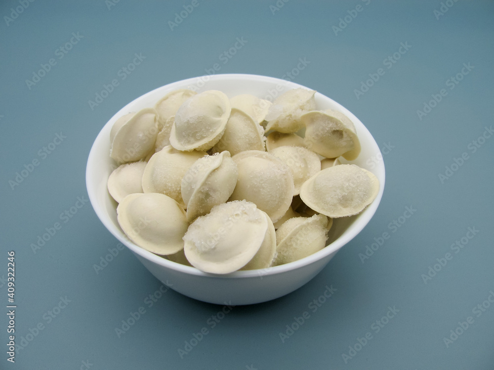 Frozen store-bought dumplings in a white bowl on a blue background.